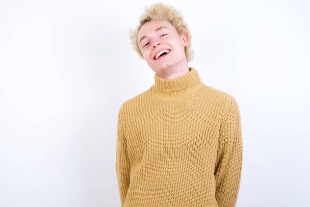 pohledný běloch blond muž stojící proti bílému pozadí se širokým úsměvem, ukazuje bílé zuby, pocit sebejistoty raduje, že den volna. - Fotografie, Obrázek