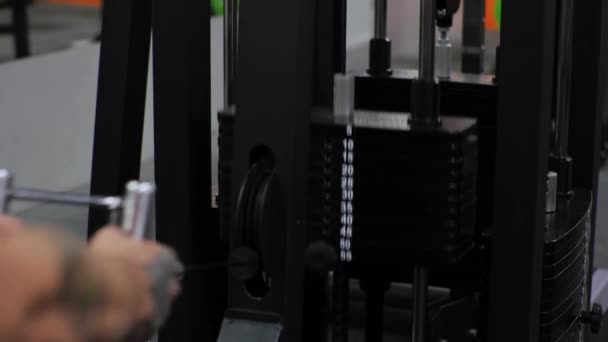 Young man works out in the gym Serious focused Shakes shoulders arms and chest on the simulator - Footage, Video