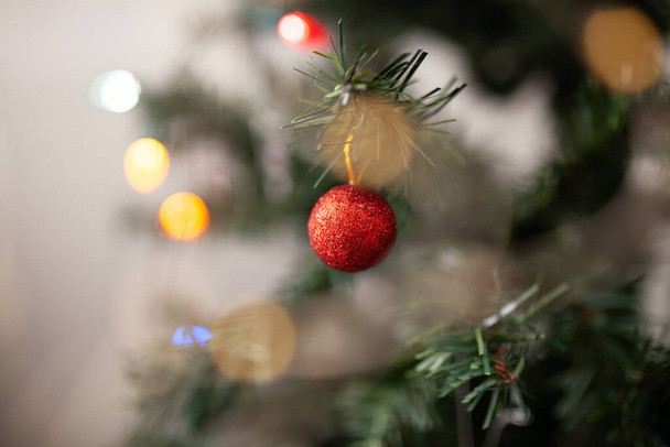 Piros kerek karácsonyfa dísz zöld ág másolási hely és vonósok fények a háttérben. Nyári üdvözlőlap. Díszített karácsonyfa közelről - Fotó, kép