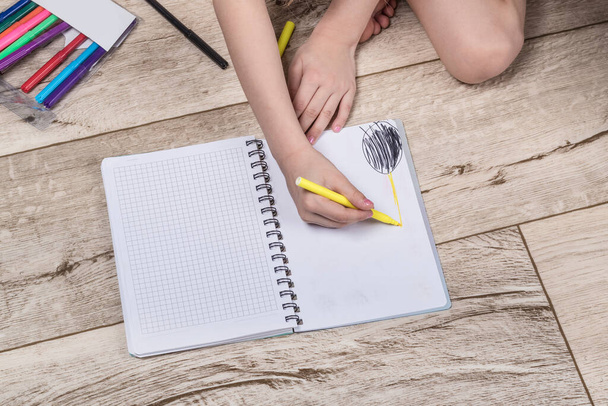 Room lighting. the child holds a pencil in his hand and draws in a notebook. Located on the floor. Close-up - Foto, Imagem