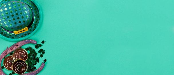 Празднование дня Святого Патрика с ирландской шляпой эльфа, ботинком лошади, золотом и мелким клевером на зеленом бумажном фоне с копировальным пространством - Фото, изображение