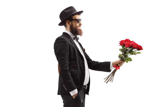 Bearded man in a suit giving a bouquet of red roses isolated on white background - Foto, afbeelding