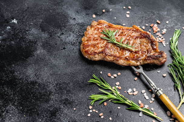 Grilled Striploin steak or strip new York on a meat fork. Black background. Top view. Copy space. - 写真・画像