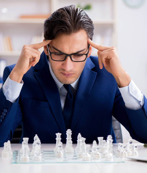 Молодой бизнесмен играет в стеклянные шахматы в офисе - Фото, изображение