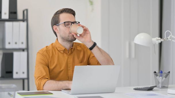 Hombre joven con el ordenador portátil de beber café en la oficina  - Foto, imagen