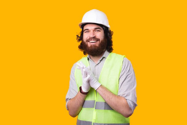 Le portrait d'un jeune architecte barbu souriant regarde la caméra portant un casque, des gants et un gilet phosphorescent. - Photo, image