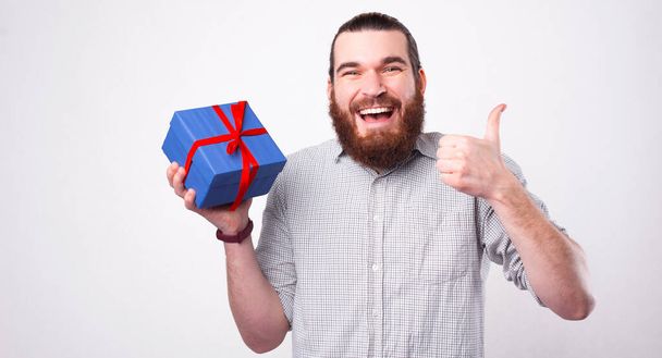 Ein fröhlicher junger Mann blickt in die Kamera und zeigt einen Daumen und dass ihm das Geschenk gefällt, das er erhalten hat - Foto, Bild