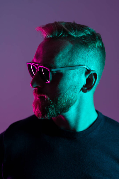 Portrait of a macho man wearing sunglasses looking away from camera. Close up shot with neon lighting. - Fotografie, Obrázek