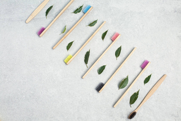 Bambusové zubní kartáčky a zelené listy na kamenném stole - Fotografie, Obrázek