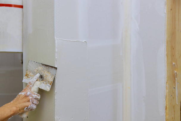 Rakentaja laittaa kipsi seinään käsi tilalla lastalla rakentamisen korjaus seinään kitti viimeistelytyöt - Valokuva, kuva