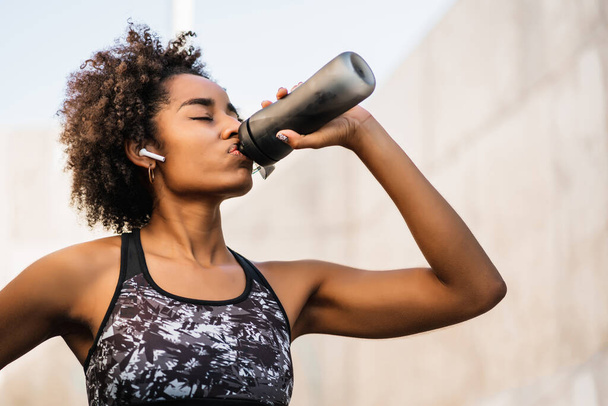 Afro atleta mujer beber agua después de hacer ejercicio al aire libre. - Foto, imagen