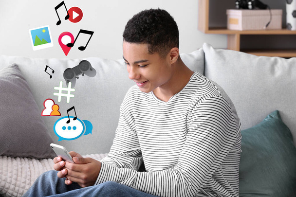 Menino adolescente afro-americano usando telefone celular para redes sociais em casa - Foto, Imagem