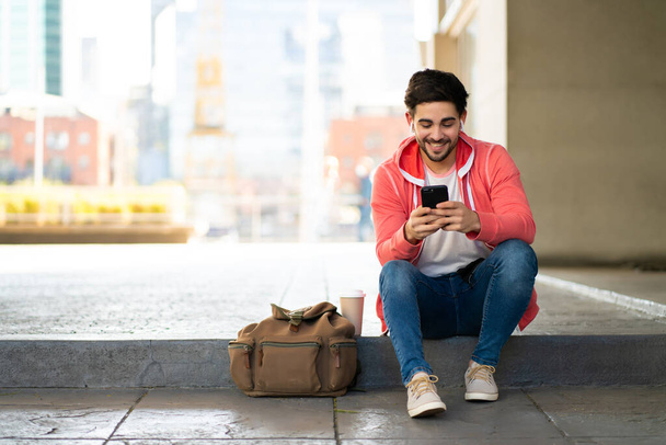 Young man using his mobile phone outdoors. - Fotó, kép