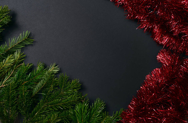 Black background with fir branches on the left corner and red tinsel to decorate the Christmas tree on the right. - Фото, зображення