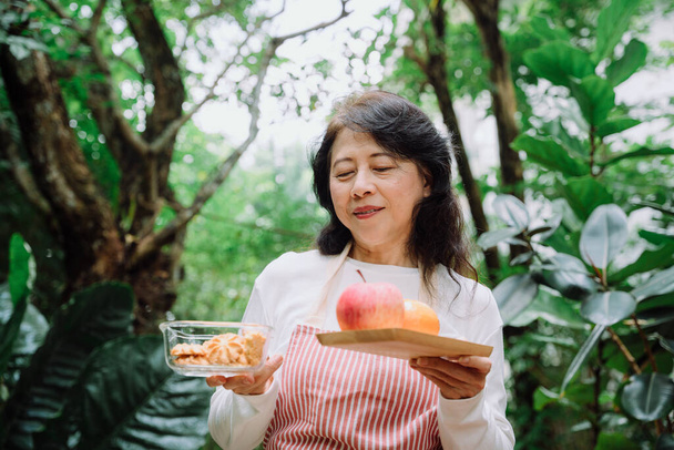 Азиатская старшая женщина завтракает печеньем и яблоком. - Фото, изображение