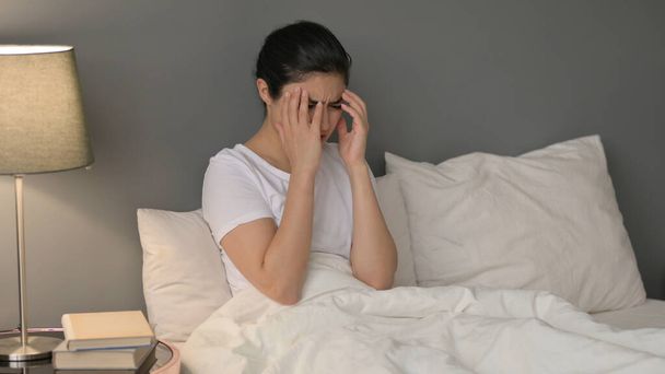 Jeune femme indienne avec mal de tête assise au lit - Photo, image