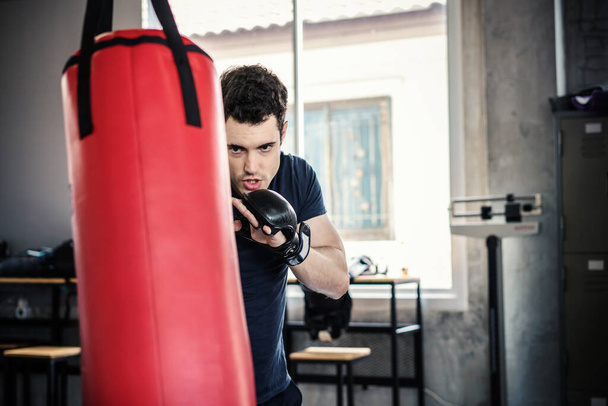 Przystojny mężczyzna w rękawiczkach bokserskich worki treningowe ćwiczenia w siłowni. - Zdjęcie, obraz