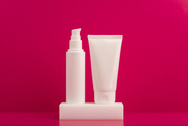 Two white unbranded cream tubes on white podium against pink background. Concept of skincare and beauty products - Foto, afbeelding