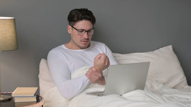 чоловік середнього віку з ноутбуком болить зап'ястя в ліжку
 - Фото, зображення