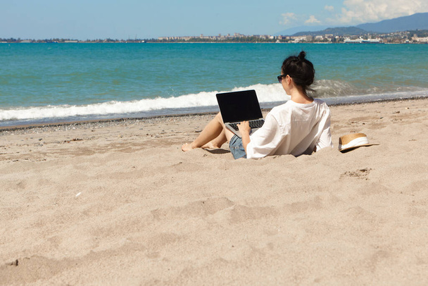 Een jonge vrouw die een laptop op het strand gebruikt. Vakantie lifestyle communicatie. Begrip freelance werk - Foto, afbeelding