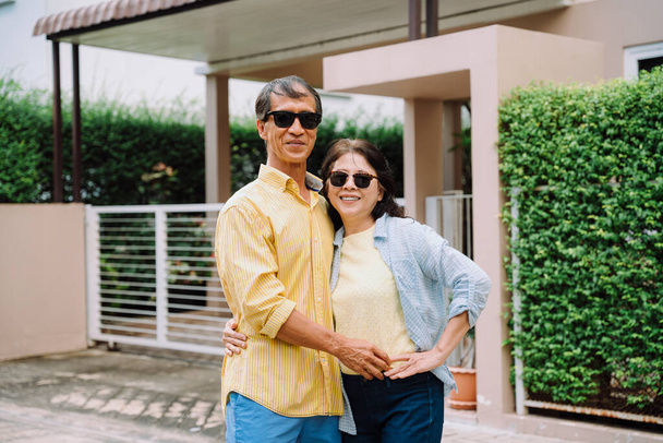 Retrato de feliz asiático casal vestindo óculos de sol de pé na frente da casa. - Foto, Imagem