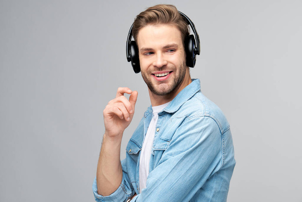 Close up portrait of cheerful young man enjoying listening to music wearing casual jeans outfit - Foto, afbeelding