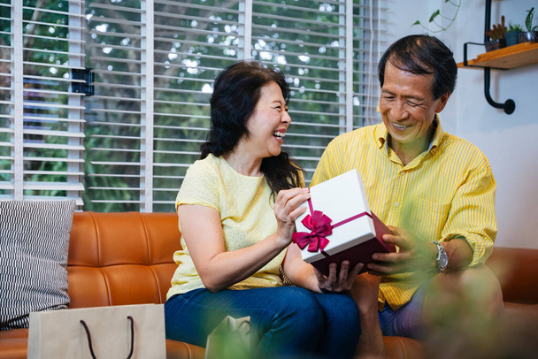 Azji senior człowiek niespodzianka jego żona dając jej prezent w Walentynki. - Zdjęcie, obraz
