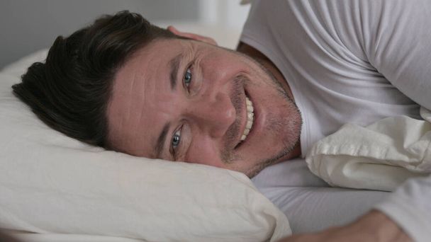 Μεσήλικας ξαπλωμένος στο κρεβάτι χαμογελώντας στην κάμερα - Φωτογραφία, εικόνα