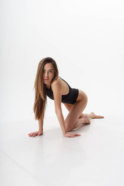sexy asian woman with long hair posing in black lingerie on white studio background with bare feet. attractive female standing on floor on her knees. model tests of skinny lady in bodysuit - Φωτογραφία, εικόνα