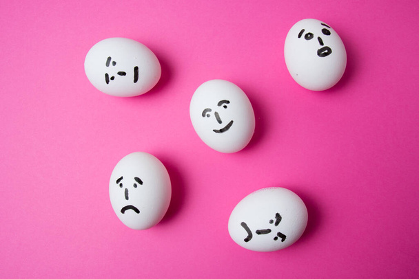 Яйца с разными лицами на розовом фоне с копировальным пространством. Концепция отношений в обществе - Фото, изображение