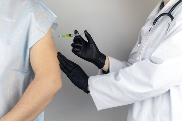 Infectious disease doctor gives the patient a medical vaccination in the shoulder. Immunization against tetanus, influenza, dysentery, whooping cough, diphtheria, measles, shigellosis and hepatitis B - Photo, Image