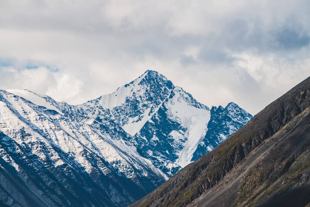 Атмосферний альпійський пейзаж до засніженого гірського хребта і крутого схилу в сонячний день. Сніг світить у денному світлі на вершині гори. Прекрасна блискуча засніжена вершина. Чудові пейзажі до низьких хмар над діапазоном
. - Фото, зображення