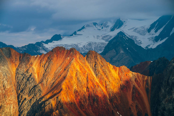 Atmospheric alpine landscape with red rockies in golden hour. Scenic view to big orange rocks and giant snowy mountains with glacier in sunrise. Wonderful highland scenery. Flying over mountains. - Photo, Image