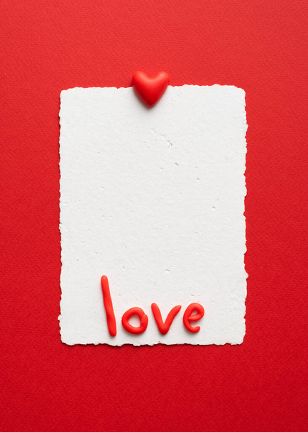 Κάρτα Αγίου Βαλεντίνου με καρδιά, νότα και λέξη αγάπης με κόκκινα γράμματα σε κόκκινο φόντο. Επίπεδη lay με αντίγραφο χώρου - Φωτογραφία, εικόνα