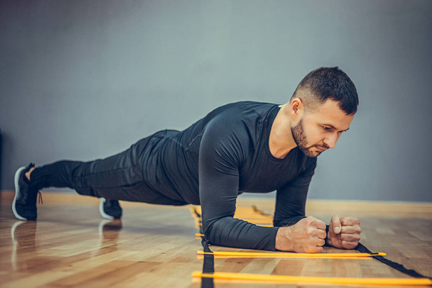 Fitness edzés sportos férfi csinál deszka gyakorlat tornaterem vagy otthon koncepció. Szakállas férfi gyakorló edzés aerob szürke háttér. - Fotó, kép