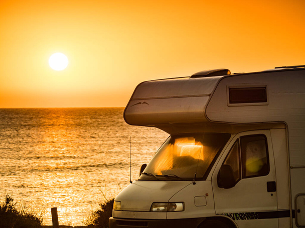 Caravan recreational vehicle camping at sunrise on beach. Vacation and traveling in motor home. - Foto, afbeelding