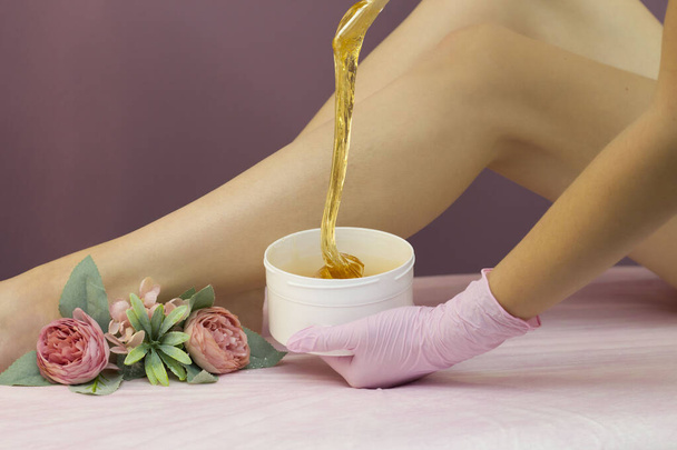 Hair removal in a luxury spa studio. Women's feet wax with saccharin. Hot sugar. The product of the wax bowl. Salon bank. Purple, lilac background - Φωτογραφία, εικόνα