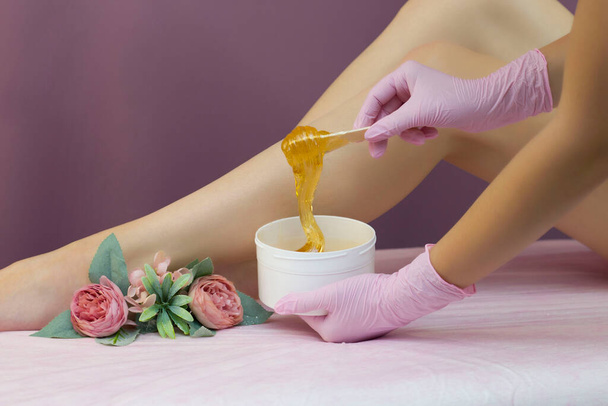 Hair removal in a luxury spa studio. Women's feet wax with saccharin. Hot sugar. The product of the wax bowl. Salon bank. Purple, lilac background - Фото, зображення