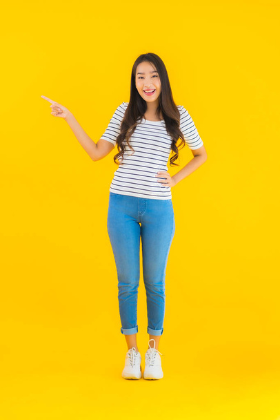 Porträt schöne junge asiatische Frau lächelt glücklich mit Aktion auf gelbem isolierten Hintergrund - Foto, Bild