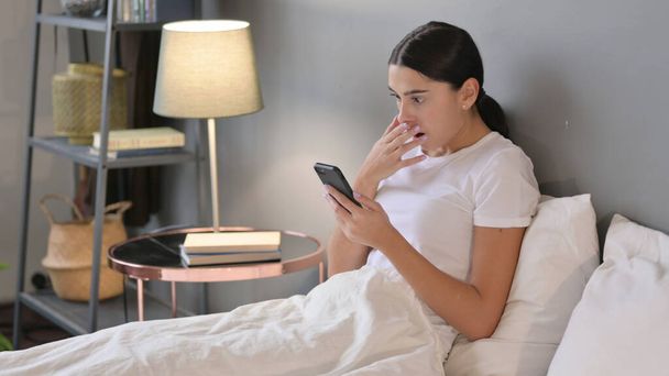 Failure, Latin Woman Reacting to Loss on Smartphone in Bed  - Foto, Bild