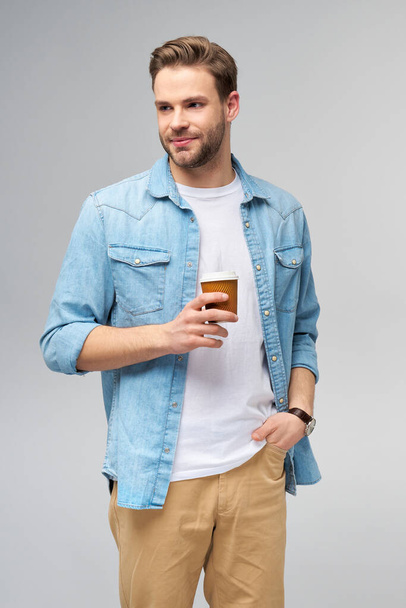 Portrait of young handsome caucasian man in jeans shirt over light background holding cup of coffee to go - Fotoğraf, Görsel