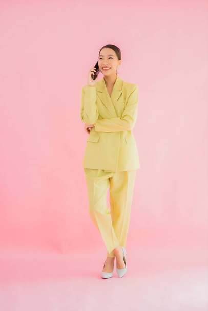 Portré gyönyörű fiatal ázsiai üzletasszony használ okos mobiltelefon csésze színes háttér - Fotó, kép
