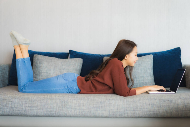 Портрет красива молода азіатка використовує комп'ютерний ноутбук на дивані в інтер'єрі вітальні
 - Фото, зображення