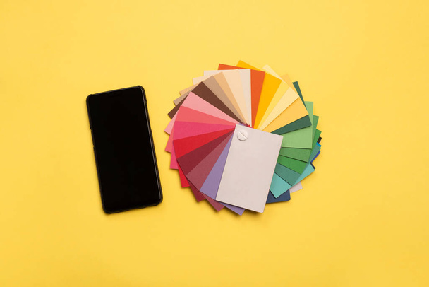 Vista dall'alto di campioni colorati e smartphone con schermo bianco su sfondo giallo - Foto, immagini