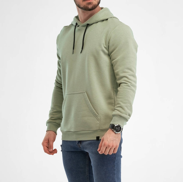 De man staat in een groene hoodie. geïsoleerde schot van bebaarde man draagt pistache kleur sweater met kap - Foto, afbeelding