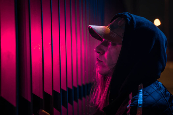 Beautiful cinematic portrait of stylish young woman in neon lighted fence. Bright neoned colors. Caucasian model, musician outdoors. Youth culture and music concept. - Zdjęcie, obraz