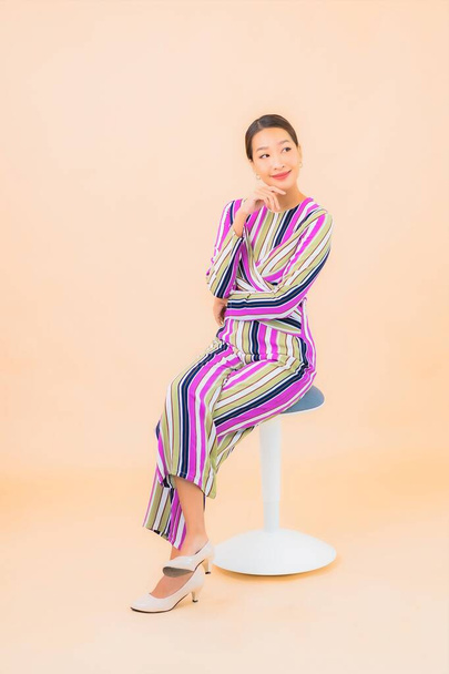 Portrét krásná mladá asijská žena sedět na židli a úsměv s akcí na barevném izolovaném pozadí - Fotografie, Obrázek