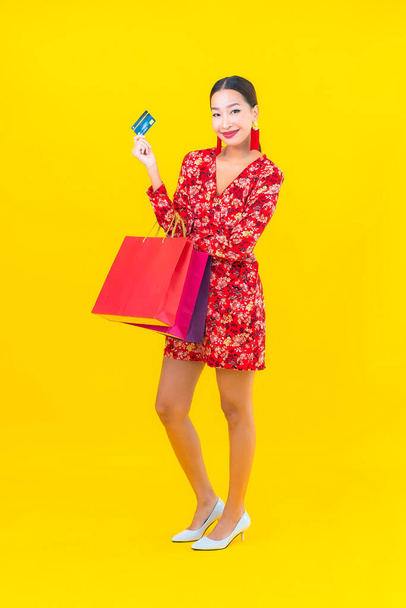 Ritratto bella giovane donna asiatica con colorata shopping bag su sfondo giallo - Foto, immagini