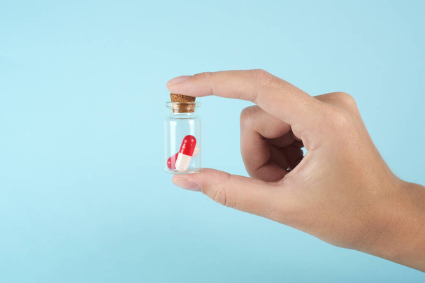 man's hand holds a glass transparent jar with pills on a light background close-up. medicines and vitamins. pharmaceuticals. chemical industry. remedies for viruses and bacteria. red and white pills - Photo, Image