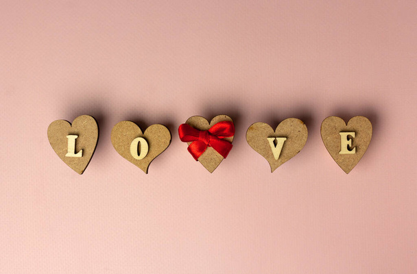 Καρδιές και λεκτική αγάπη φτιαγμένη από ξύλινα γράμματα σε ροζ φόντο. Του Αγίου Βαλεντίνου. Έννοια αγάπης καρδιάς. Ευχετήρια κάρτα. Επίπεδο lay, αντίγραφο χώρου. - Φωτογραφία, εικόνα